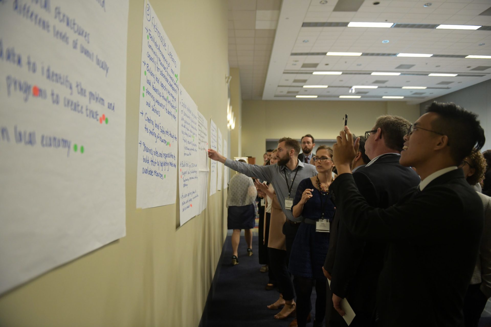 Participants standing at a wall. Wall covered in poster paper where participants are jotting down notes.