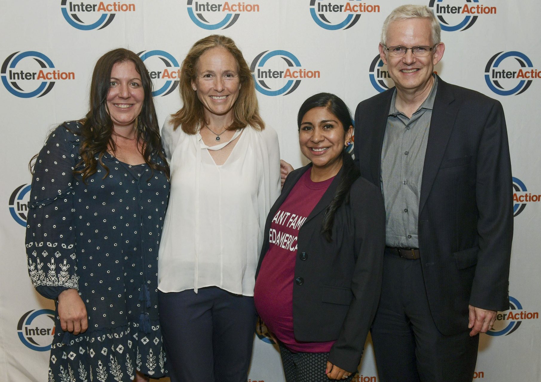 three women and a man pose for a photo in front of a step and repeat