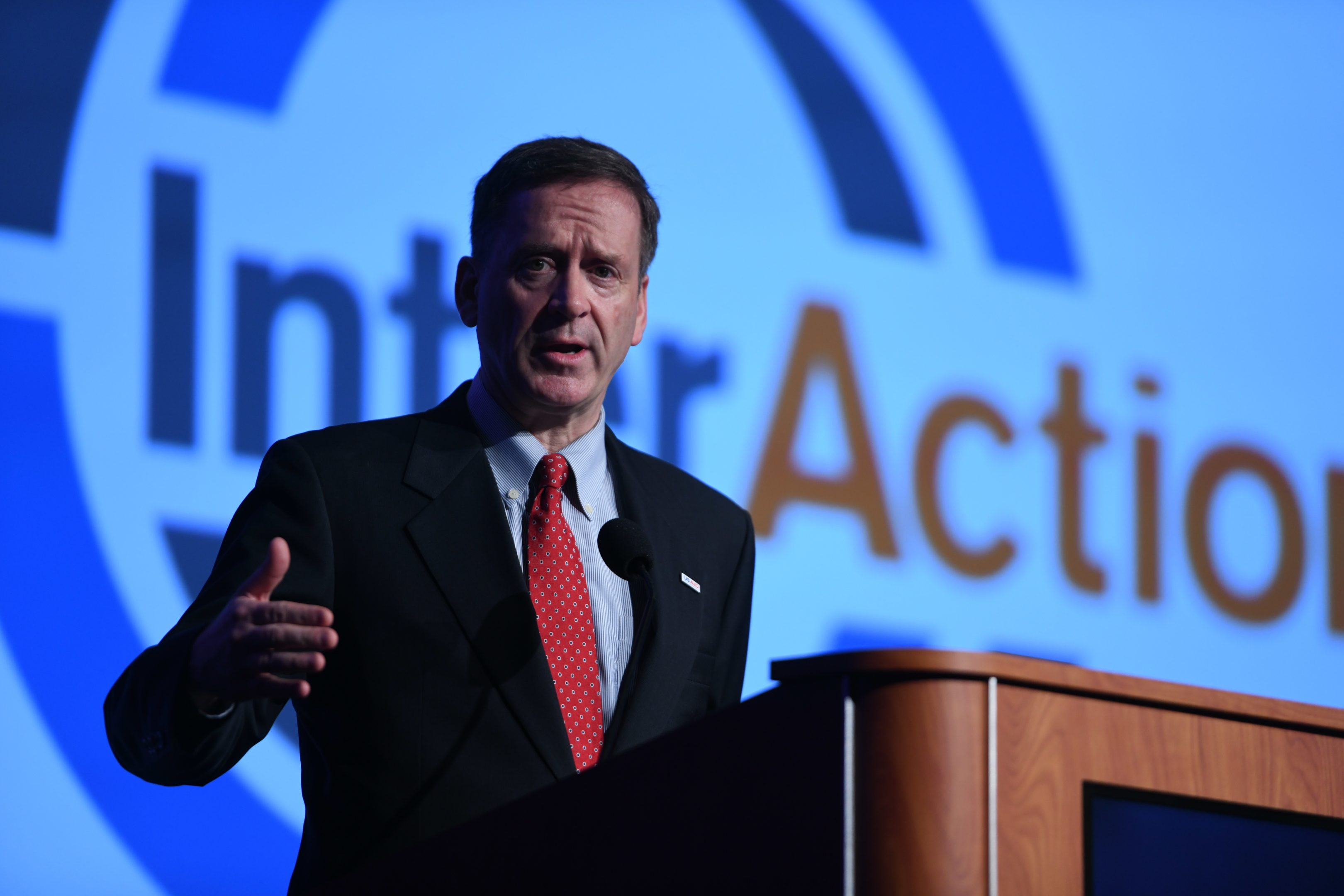 USAID Administrator Mark Green speaks on stage, looking out the left at the audience, at the podium during InterAction Forum.
