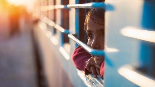 Small child peers out the window of a train during dusk.