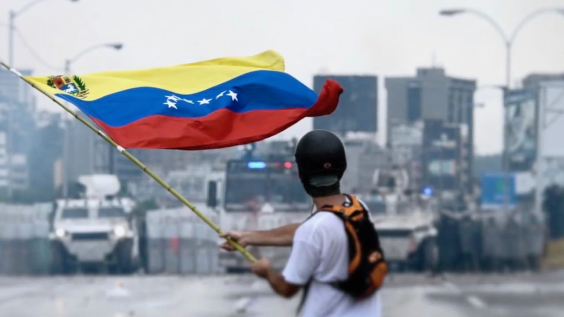 Young protester stands in the middle of a highway waving a Venezuelan flag