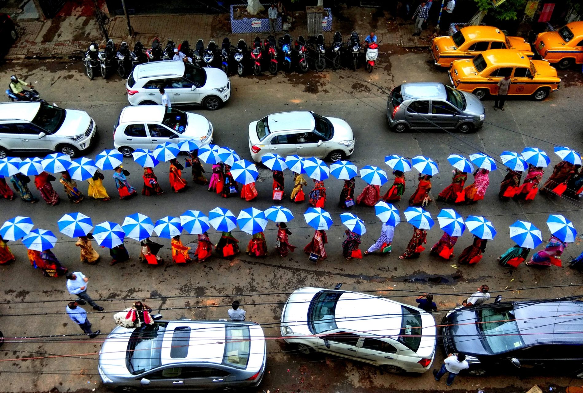 People march through a street, in two lines, holding up blue and white