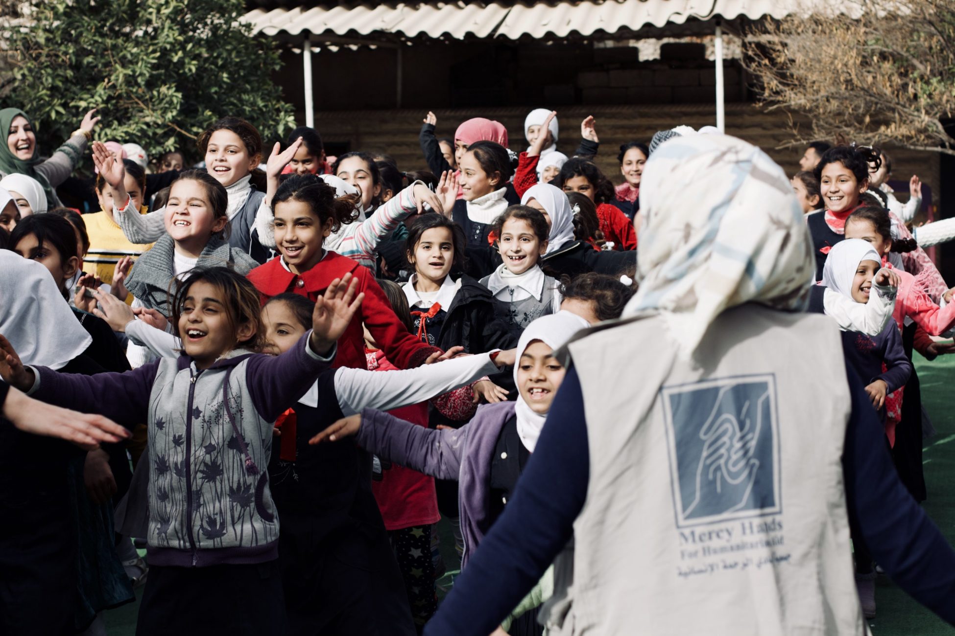 An aid working stands in front of group of smiling children in Mosul.