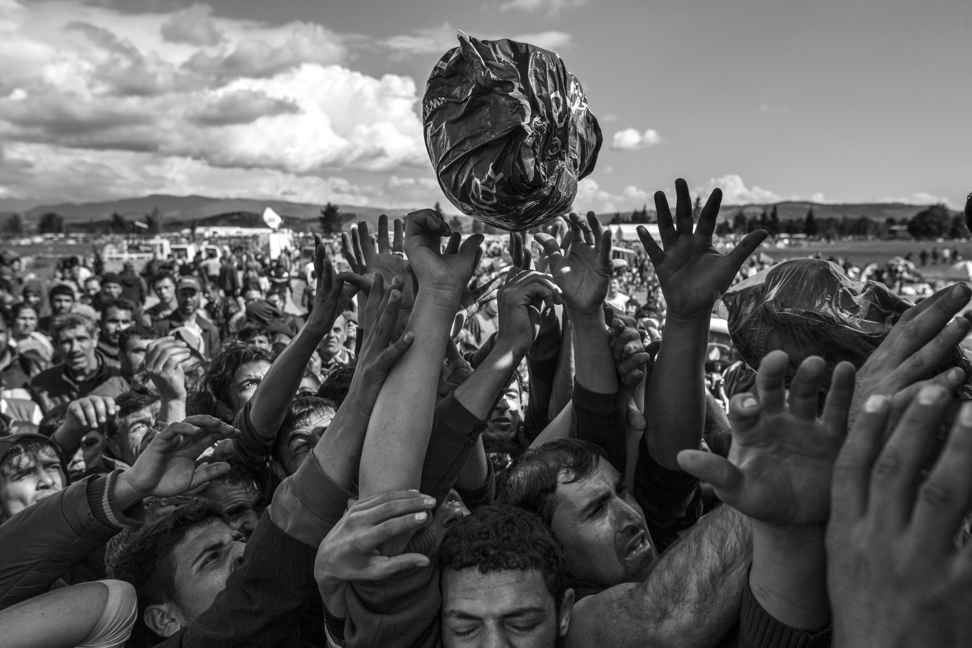 Hands reach for a package of food rations amid a large crowd of refugees