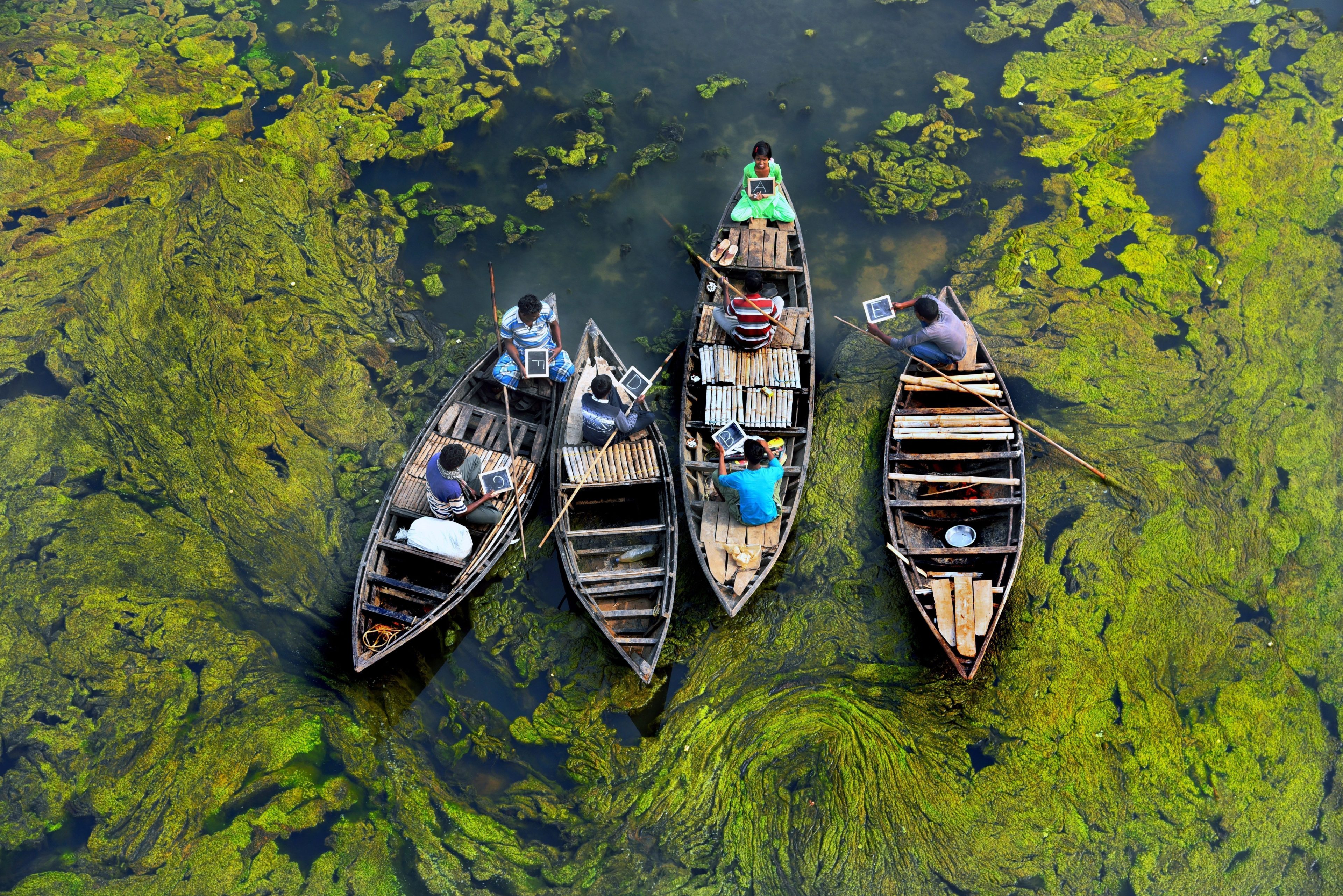 Four boats sitting in a marsh, holding students as they read from there books during a school lesson.