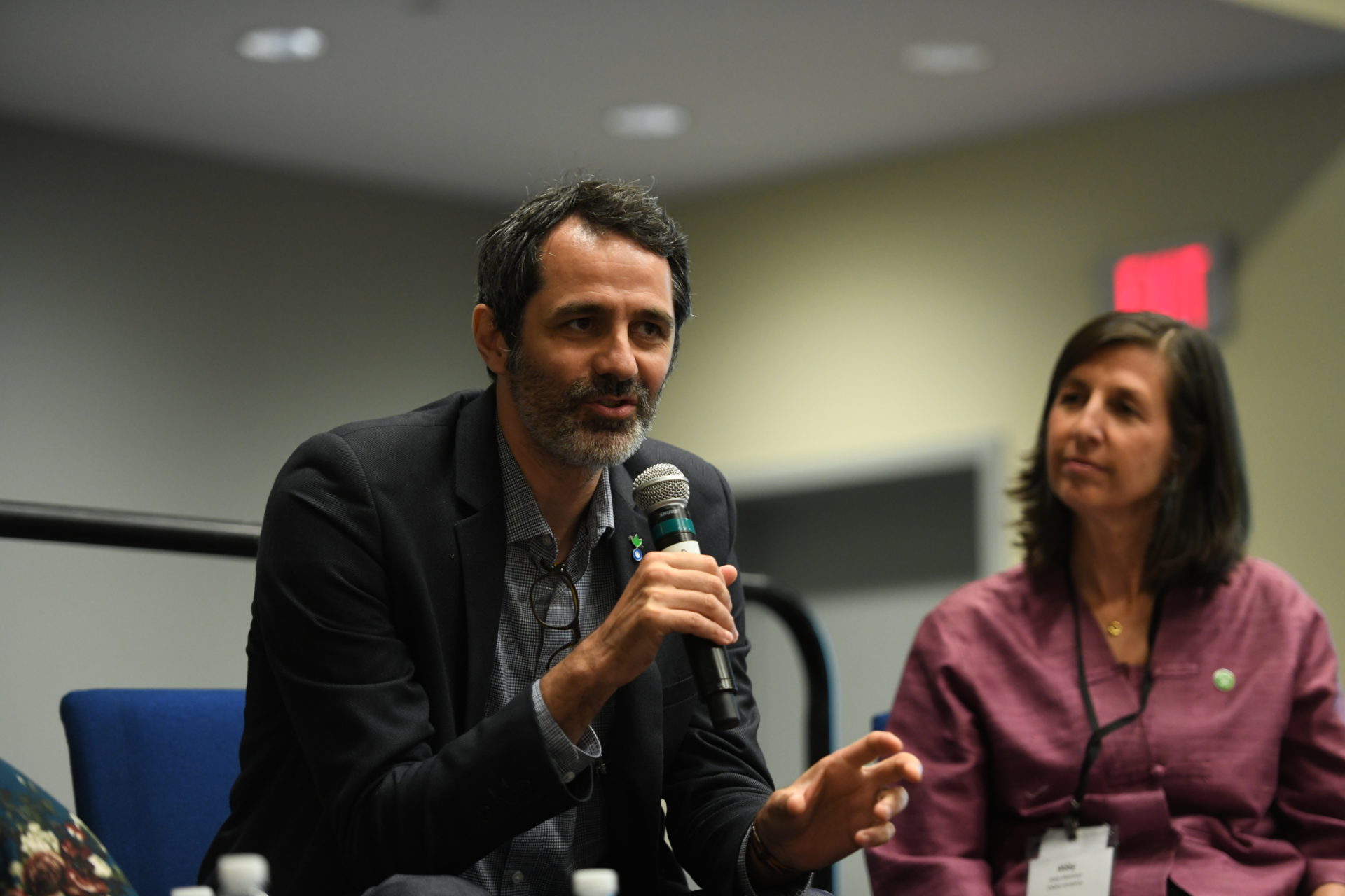 Two InterAction members sitting on stage, the male on the left is holding a mic and the woman on the right is looking at him while deep in thought.