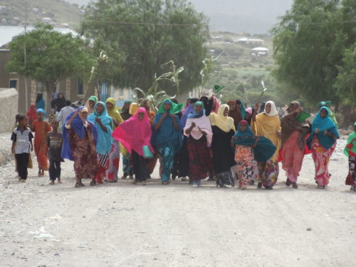 A group of women march happily down a dirt road