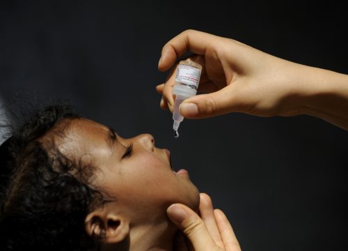 An adult administers a vaccine dose into the mouth of a child
