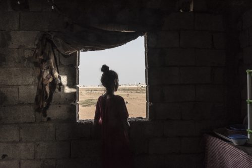 A young girl looks out the open window of a home