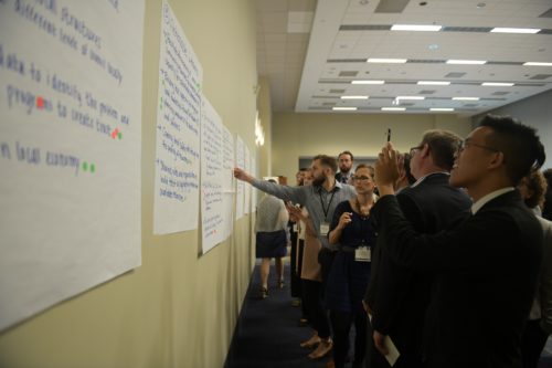 A group of men and women look at posters attached to a wall, discussing feedback.