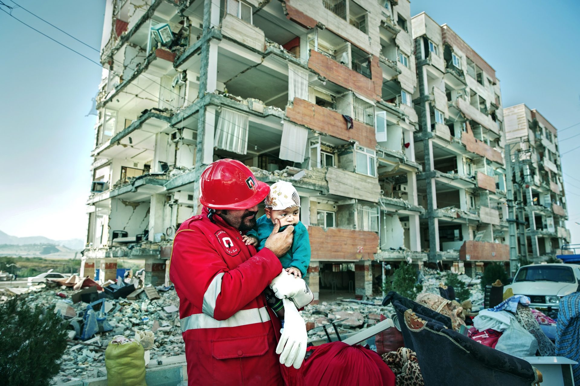 A rescue worker hold a small injured child in front of a partially destroyed apartment building