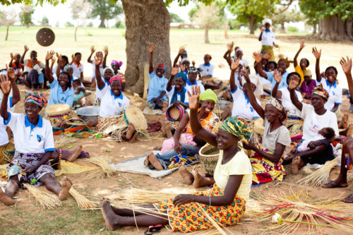 A group of women sit on the ground making baskets