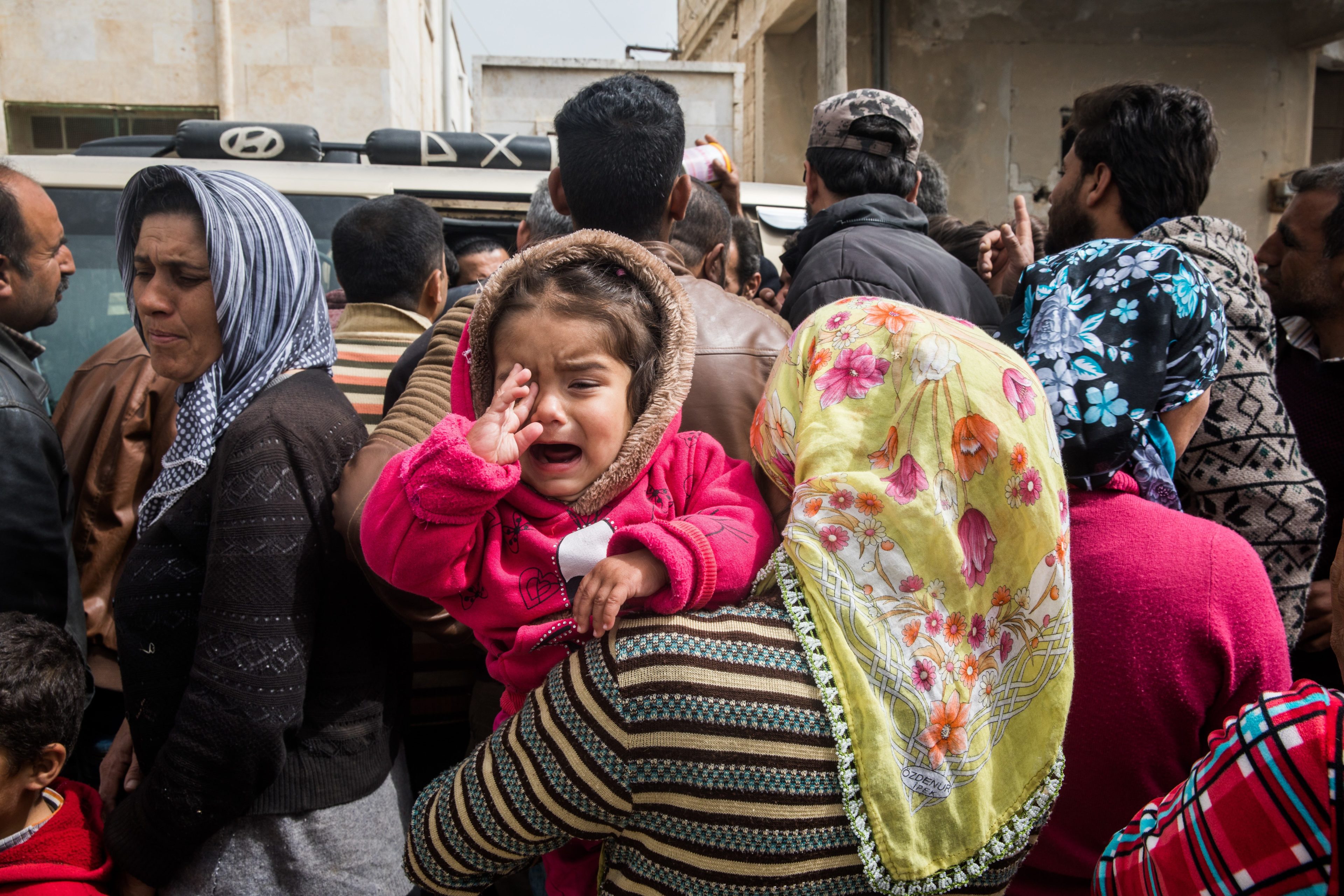 Woman holding her crying child in a crowd of people looking to find transport out of Afrin Syria