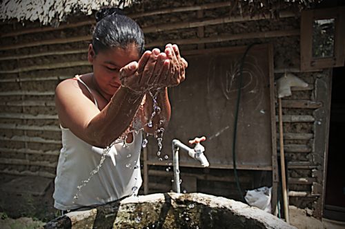 Young girl standing over a well, cups water in her hand and it slowly drips out