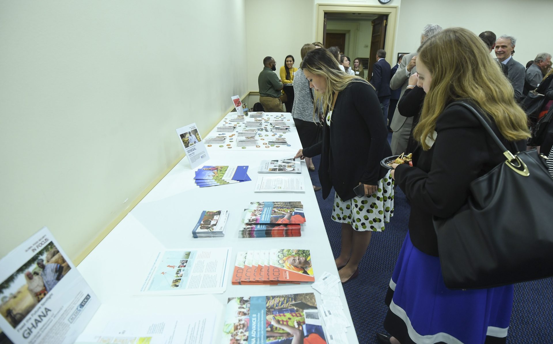 people gather around an information table that includes pamphlets and brochures