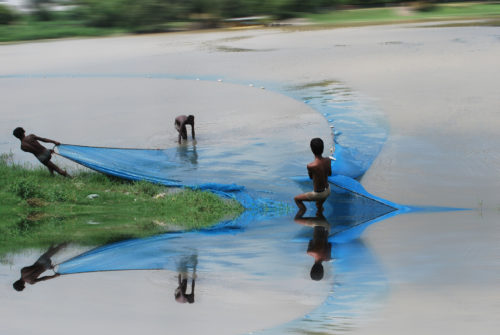 Two men pull a blue fishing net out of the water
