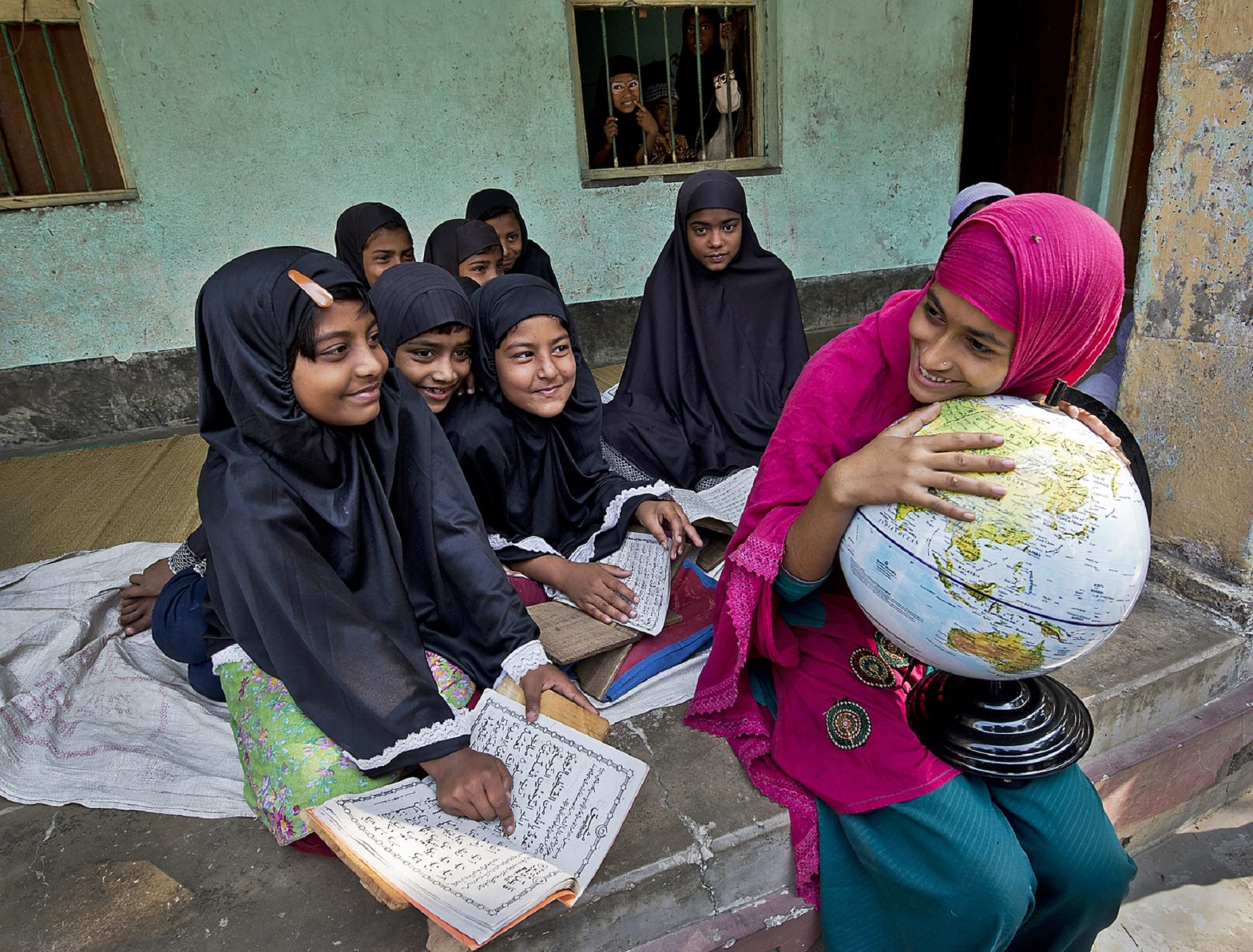 Girls reading and laughing. One girl holds to a globe