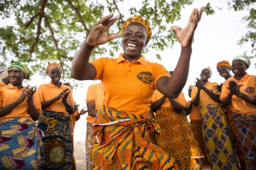 Members of CRS-supported SILC groups (Savings and Internal Lending Communities) dance together during a meeting in Awaradoni village, Upper East Region, Ghana. These women have begun making and selling shea nut butter, straw baskets, and parboiled rice ever since interrupted weather patterns related to climate change have inhibited their abilities to earn livelihoods through farming. Awaradoni village, Talensi District, Upper East Region, Ghana, West Africa. March 19, 2016 - Photo by Jake Lyell for CRS.