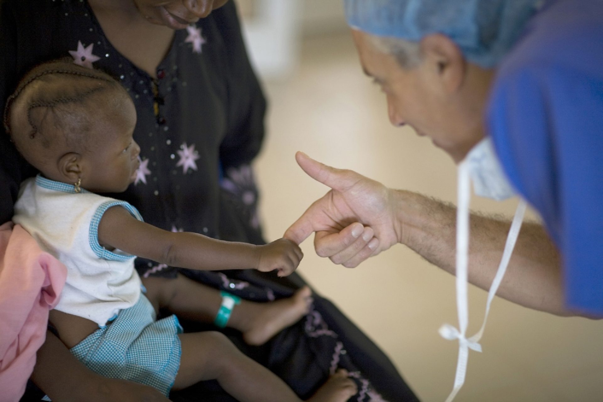 doctor holds finger of small child sitting in her mother's lap