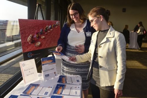 two women stand at a table looking at reading materials.