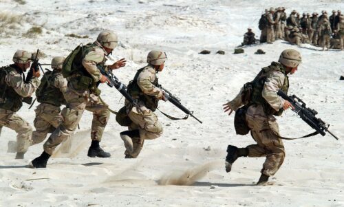 A group of soldiers run across the sand in what appears to be a military exercise